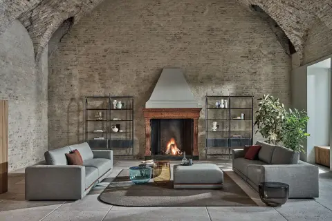 Scegliere tappeto salotto: un'elegante zona living con divani grigi, camino acceso e tavolini moderni su un tappeto rotondo.