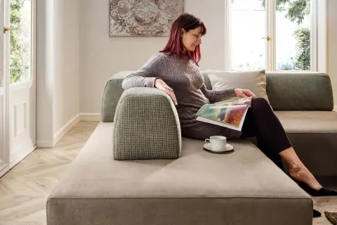 Donna legge su un divano centro stanza piccola, con tazza di caffè.