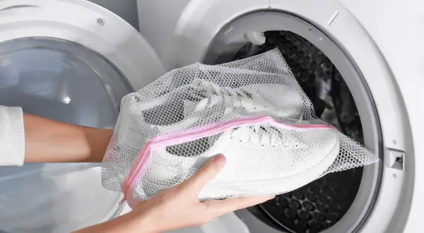 Mani inseriscono scarpe bianche in una retina per lavatrice, un modo semplice per capire come lavare le scarpe in lavatrice.