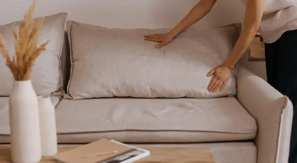 Mani che sistemano un cuscino su un divano beige, un'idea per rivestire divano fai da te.