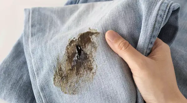 Macchia scura su tessuto di jeans, simile a muffa su tessuti, che rovina il capo.
