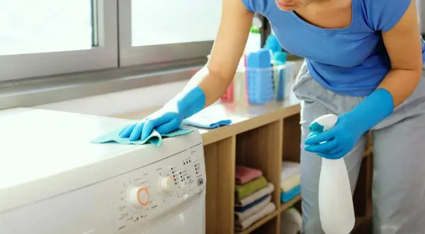Donna con guanti blu pulisce la lavatrice. Effettua il primo lavaggio lavatrice a vuoto per igienizzarla.