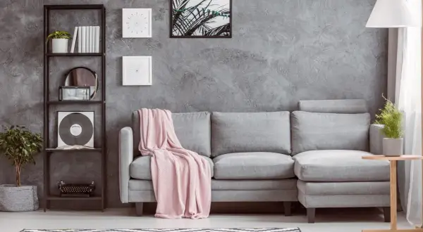 Un divano grigio con coperta rosa, libreria nera con piante e vinile, e un tavolino di legno: idee su cosa mettere vicino al divano per un tocco moderno.