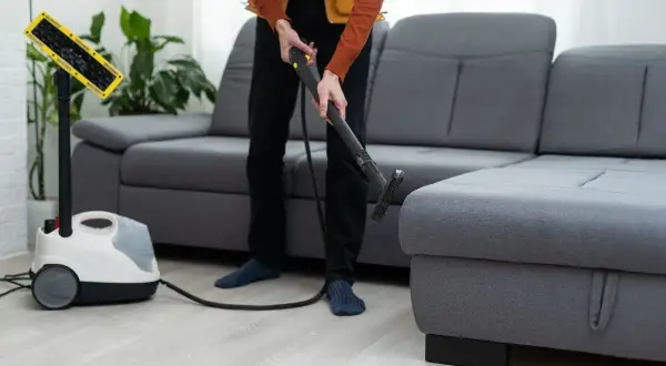 Pulizia profonda del divano Poltronesofà con un pulitore a vapore. Un professionista usa l'accessorio per igienizzare il tessuto.