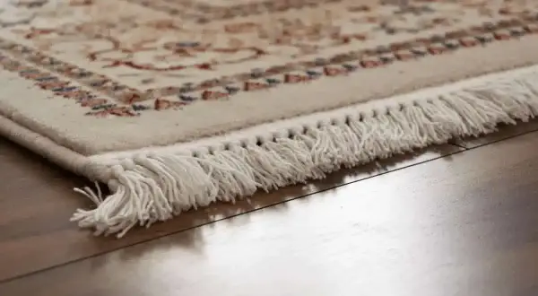 Dettaglio di un tappeto con frange bianche su parquet lucido. Scopri come pulire i tappeti per mantenerli splendenti.