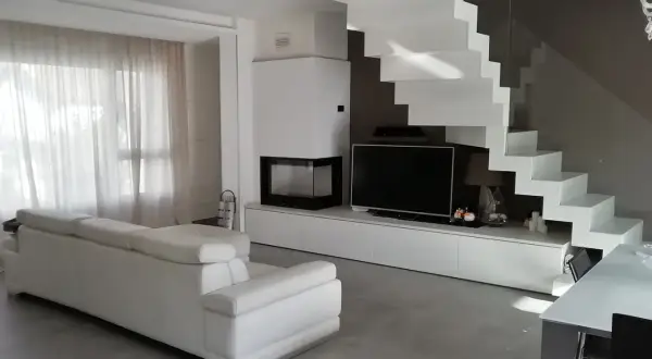 Soggiorno moderno con divano bianco, camino, TV e una scenografica scala a vista bianca. Ottime idee arredare soggiorno con scala a vista.