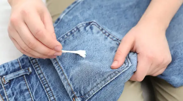 Mani che rimuovono la cingomma dai jeans con un cotton fioc. Ecco come togliere la cingomma dai vestiti.