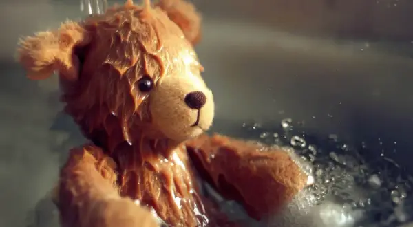 Orsetto di peluche bagnato, con gocce d'acqua che scendono. Una scena che ricorda come lavare i peluche in lavatrice per farli tornare come nuovi.