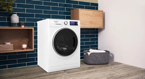 Lavatrice Hotpoint con funzione Steam Care, che significa cura delicata dei tessuti. Ambiente moderno con dettagli in legno e piastrelle blu.