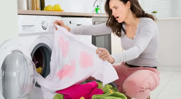 Donna scopre con orrore macchie rosse su un capo bianco appena lavato, un classico problema di come eliminare le macchie da trasferimento di colore rosso.