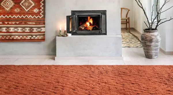 Un tappeto decorativo con motivi geometrici arancioni e bianchi è appeso al muro, un'idea per come appendere un tappeto al muro.