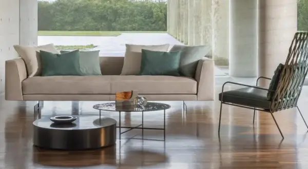 Divano 3 posti beige con cuscini verdi, tavolini rotondi e poltrona di design in un soggiorno moderno.