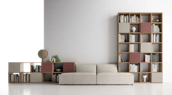 Un comodo divano beige è posizionato davanti a una libreria modulare in legno, piena di libri e oggetti decorativi.