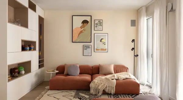 Un accogliente soggiorno con un divano color terracotta e un tappeto su parquet chiaro. Decorazioni alle pareti e una libreria a muro completano l'ambiente.