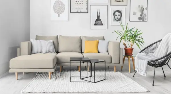 Divano componibile beige con cuscini decorativi, tavolini neri e poltrona nera. Idee su come rivestire un divano non sfoderabile.