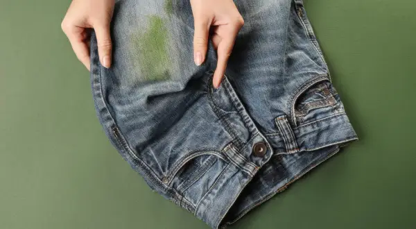 Mani che indicano una macchia verde su jeans, per mostrare come togliere macchie di jeans su ecopelle.