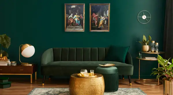 Elegante soggiorno con divano verde, tavolini dorati e due quadri classici che creano un contrasto moderno.