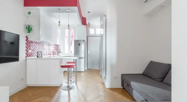Un accogliente open space di 20 mq con cucina moderna, divano grigio e dettagli rossi vivaci.
