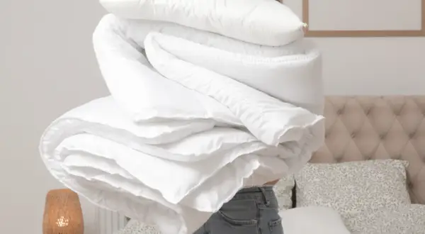 Donna con un grande piumone bianco, pronto per lavare copriletto in lavatrice. La biancheria da letto è piegata in modo ordinato.