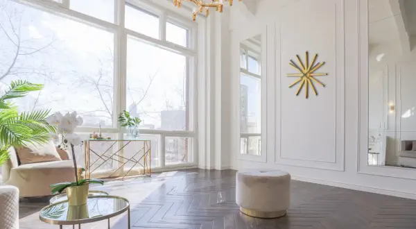 Un elegante soggiorno con un tavolino rotondo dorato, un pouf beige e un orologio a muro dorato a forma di sole.
