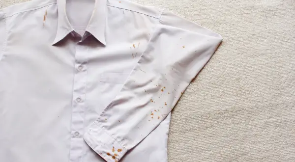 Camicia bianca con macchie di ruggine vecchie sui tessuti, soprattutto sulla manica e sul colletto.