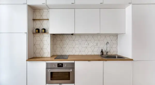 Moderna cucina bianca con paraschizzi a esagoni geometrici, piano in legno e forno in acciaio.