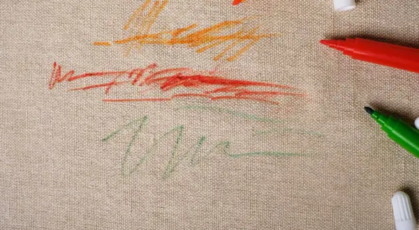 Tracce di pennarelli colorati su tela grezza, con macchie di pennarello secche che raccontano un momento creativo.