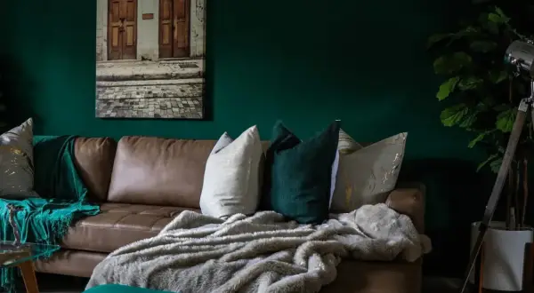 Divano in pelle marrone con cuscini decorativi e coperte morbide, che creano un'atmosfera accogliente. Diversi tipi di pelle e tessuto si combinano per un look sofisticato.