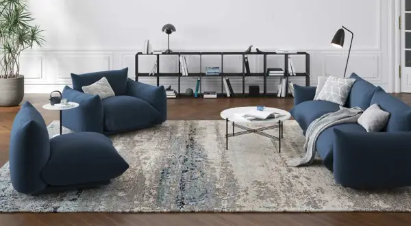 Un ampio tappeto 3 metri con motivi astratti grigi e blu, che completa un salotto moderno con divani blu e tavolino bianco.