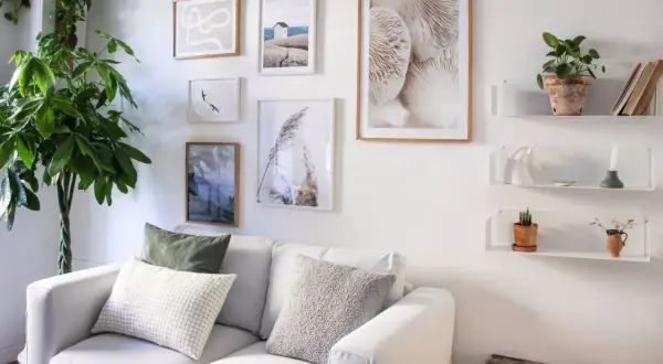 Galleria di quadri e mensole bianche sopra un divano bianco, con piante e oggetti decorativi. Idee mensole sopra divano per un tocco di stile.