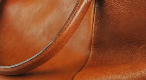Dettaglio di una borsa in pelle marrone, con la texture del materiale che mostra lievi graffi sulla pelle, testimoni di un uso vissuto.