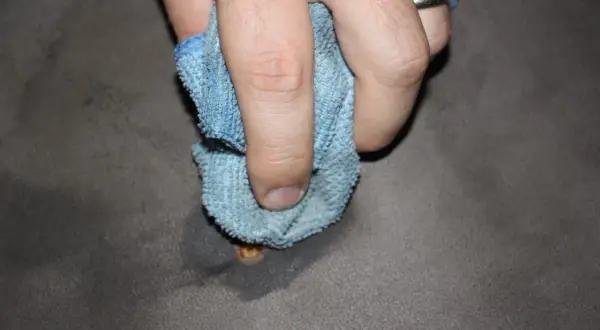 Mano che pulisce una bruciatura da sigaretta su tessuto grigio con un panno blu.