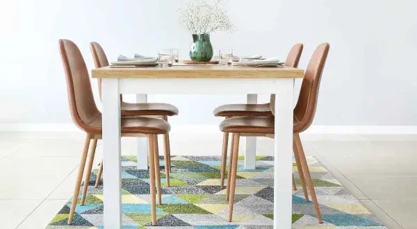 Tappeto sotto il tavolo da pranzo: sì! Un tappeto geometrico colorato aggiunge stile e comfort alla zona pranzo con sedie in pelle marrone.