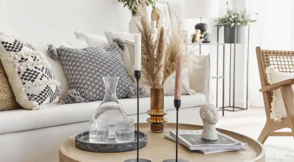 Un accogliente salotto bohemien con cuscini decorati, un vaso di erba della pampa e un tavolino con oggetti d'arte.