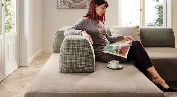 Donna legge su un divano centro stanza piccola, con tazza di caffè.