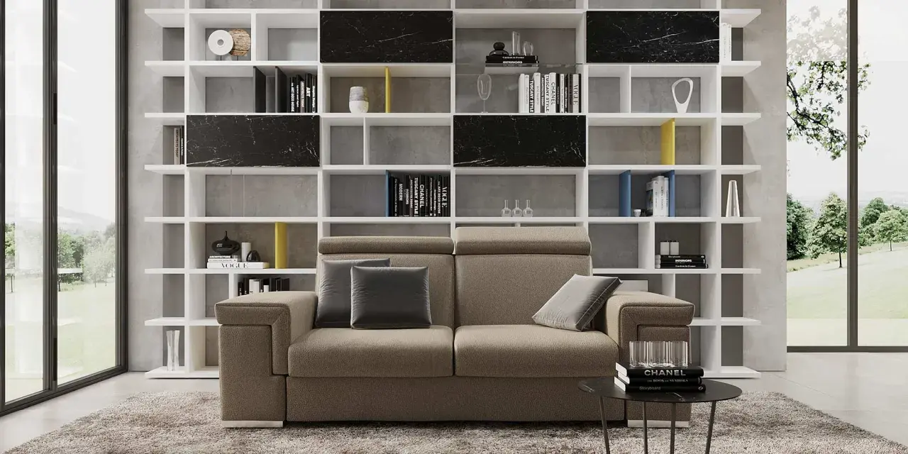 Divano moderno in un soggiorno ampio, con libreria bianca a giorno piena di libri e oggetti d'arte.