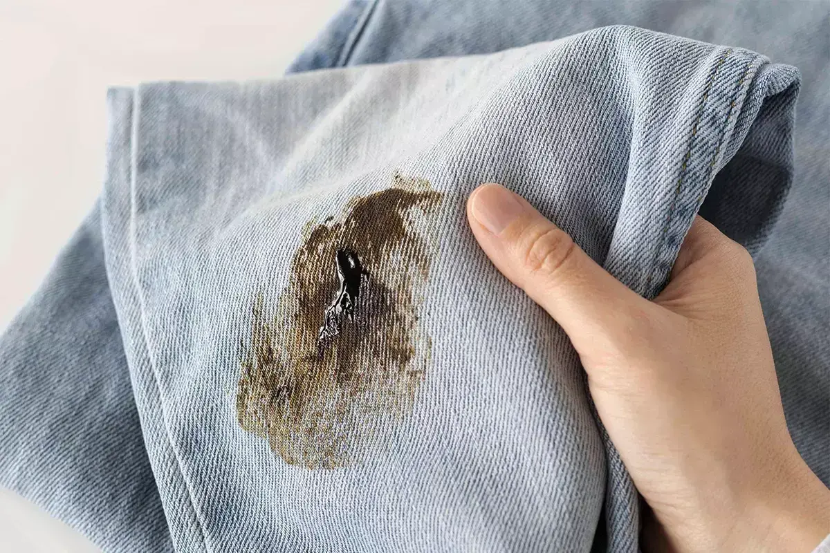 Macchia scura su tessuto di jeans, simile a muffa su tessuti, che rovina il capo.
