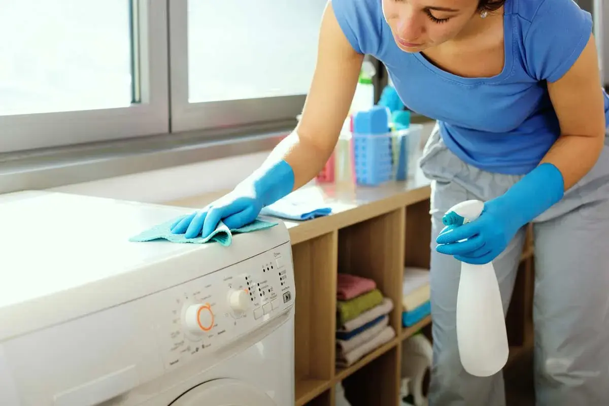 Donna con guanti blu pulisce la lavatrice. Effettua il primo lavaggio lavatrice a vuoto per igienizzarla.