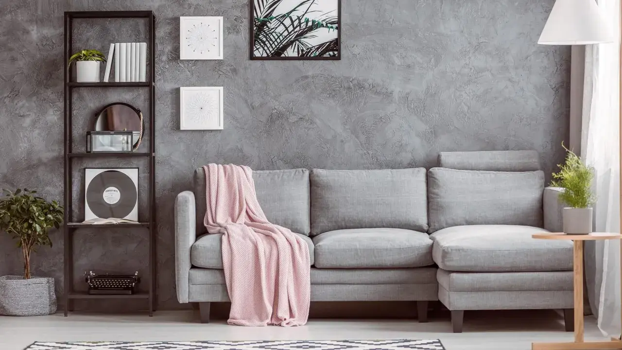Un divano grigio con coperta rosa, libreria nera con piante e vinile, e un tavolino di legno: idee su cosa mettere vicino al divano per un tocco moderno.