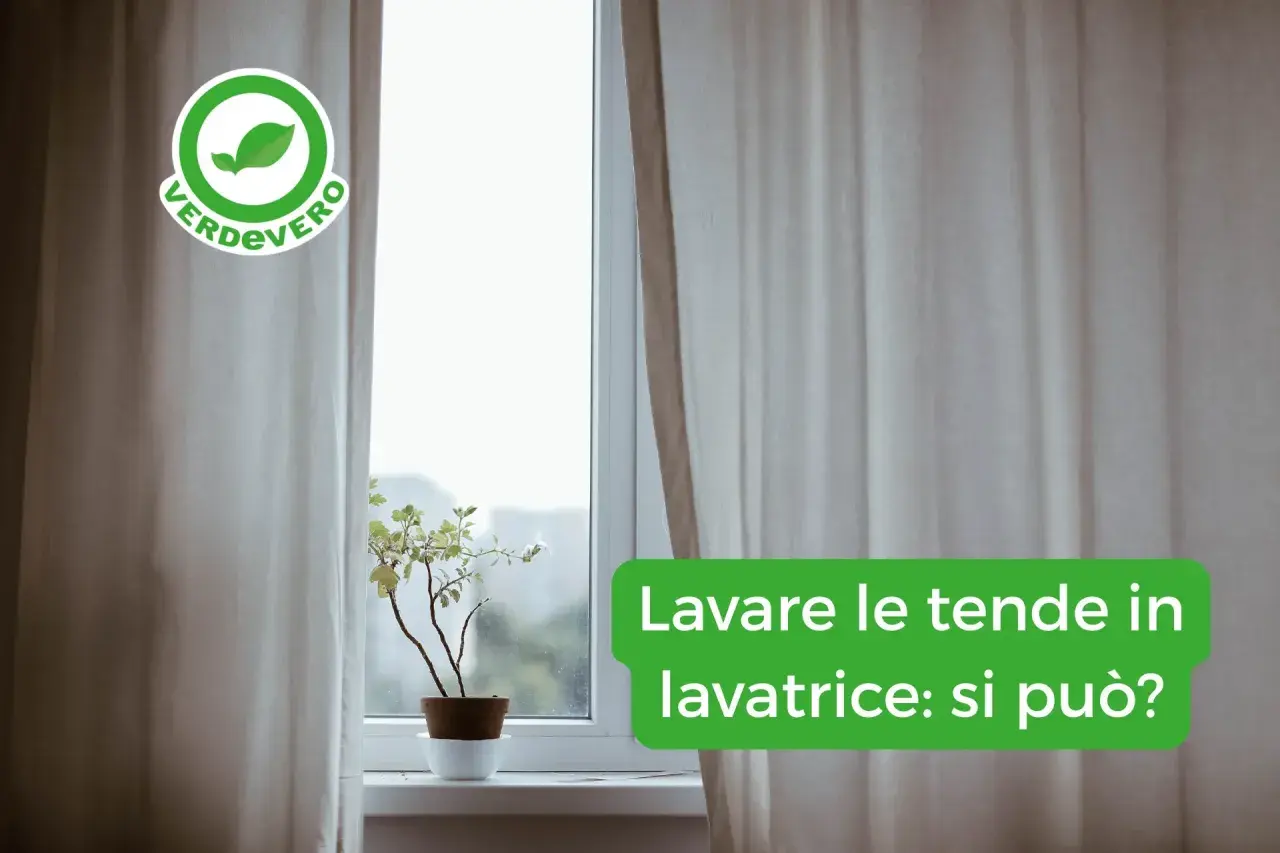 Tende chiare drappeggiate accanto a una finestra con una pianta in vaso. Il testo sovrapposto chiede: "Lavare le tende in lavatrice: si può?".