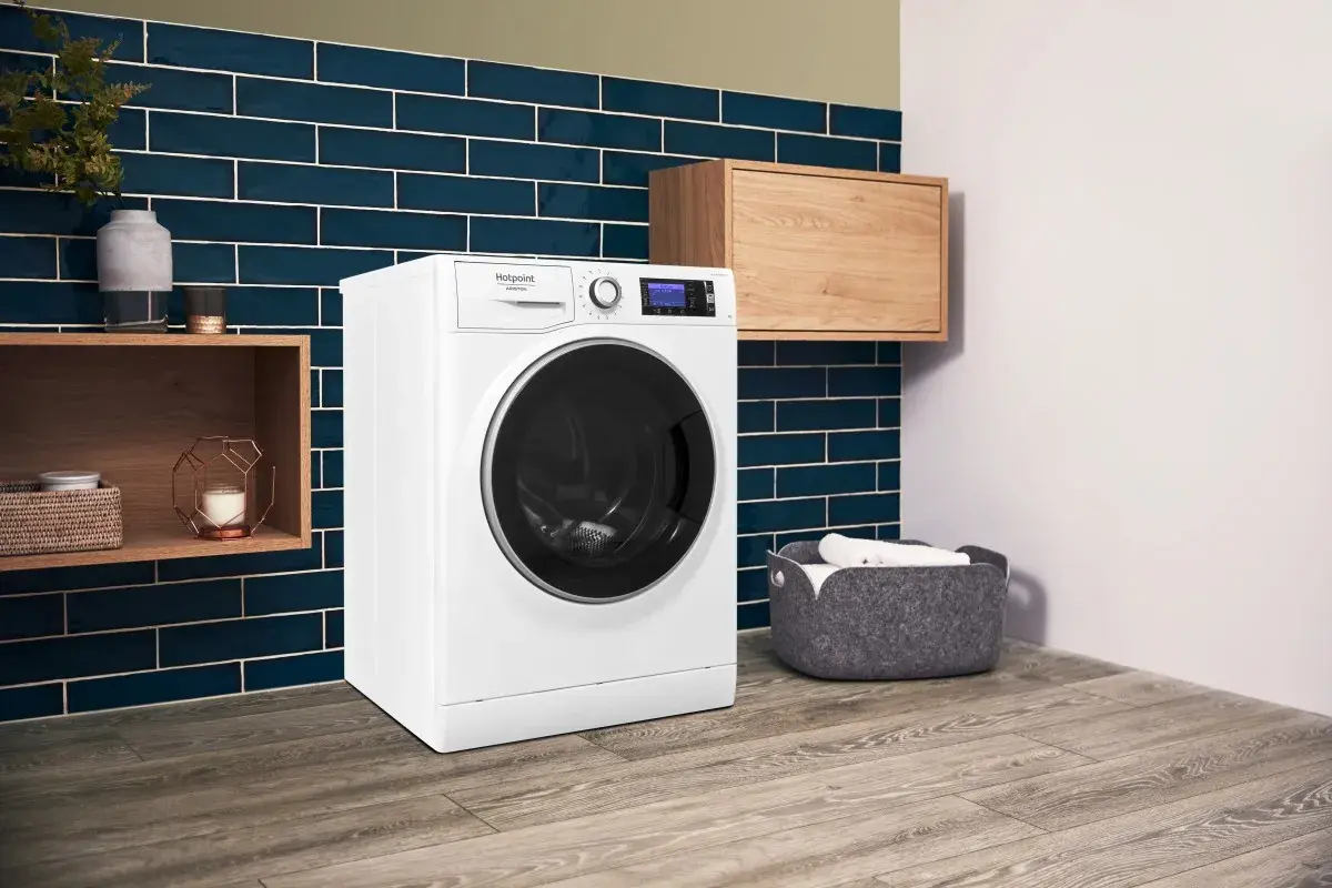 Lavatrice Hotpoint con funzione Steam Care, che significa cura delicata dei tessuti. Ambiente moderno con dettagli in legno e piastrelle blu.