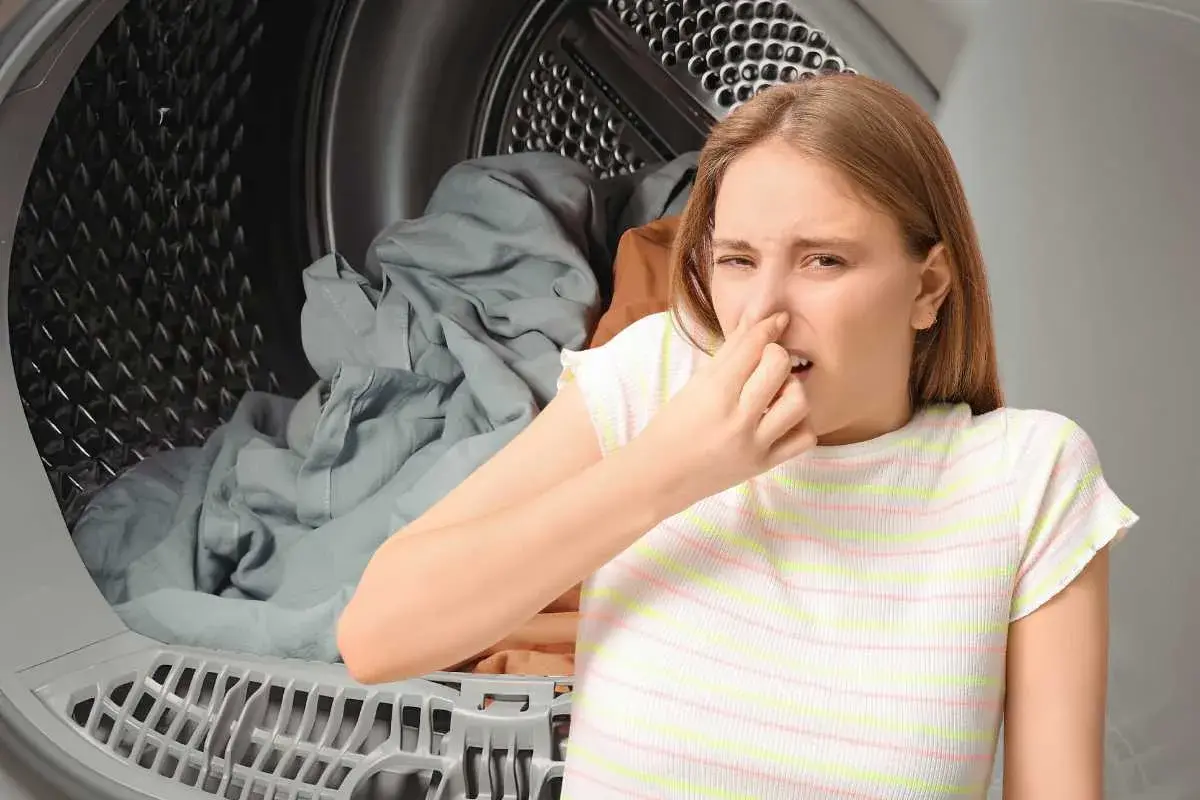 Ragazza con espressione disgustata che si tappa il naso davanti a panni in asciugatrice tutta la notte.