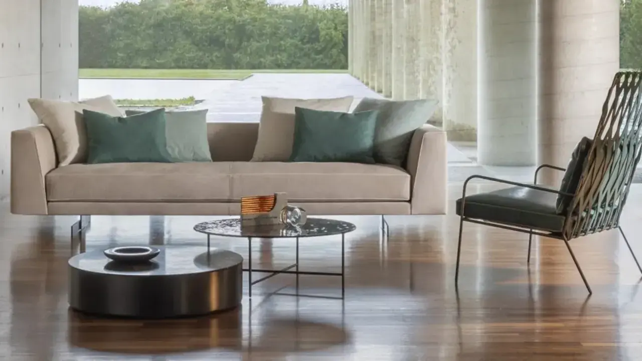 Divano 3 posti beige con cuscini verdi, tavolini rotondi e poltrona di design in un soggiorno moderno.