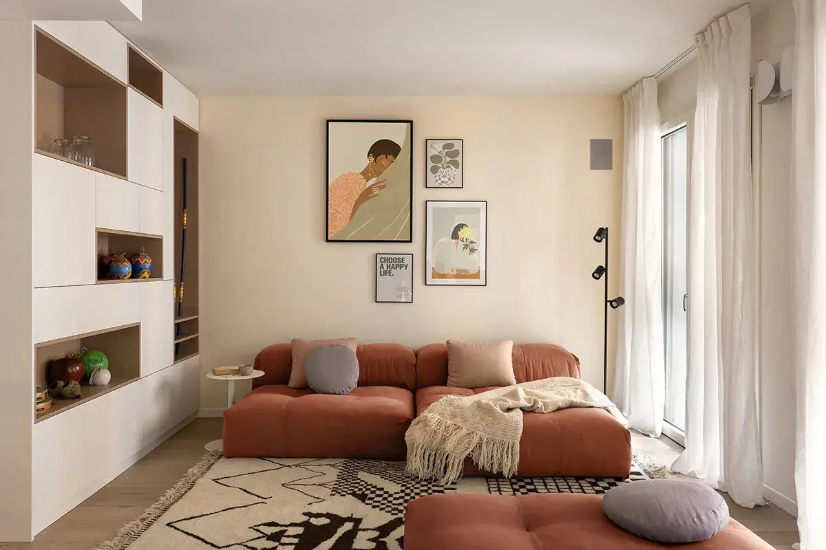 Un accogliente soggiorno con un divano color terracotta e un tappeto su parquet chiaro. Decorazioni alle pareti e una libreria a muro completano l'ambiente.