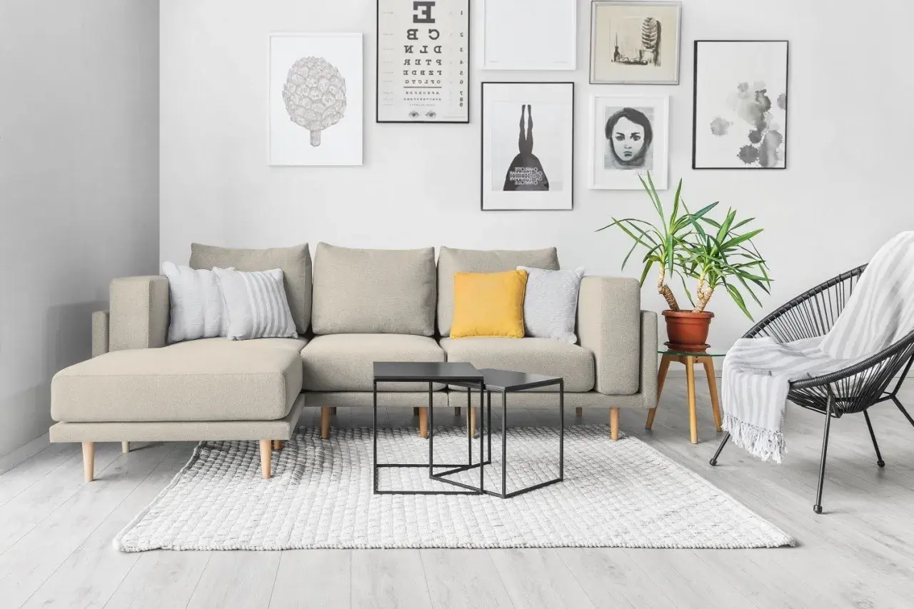Divano componibile beige con cuscini decorativi, tavolini neri e poltrona nera. Idee su come rivestire un divano non sfoderabile.