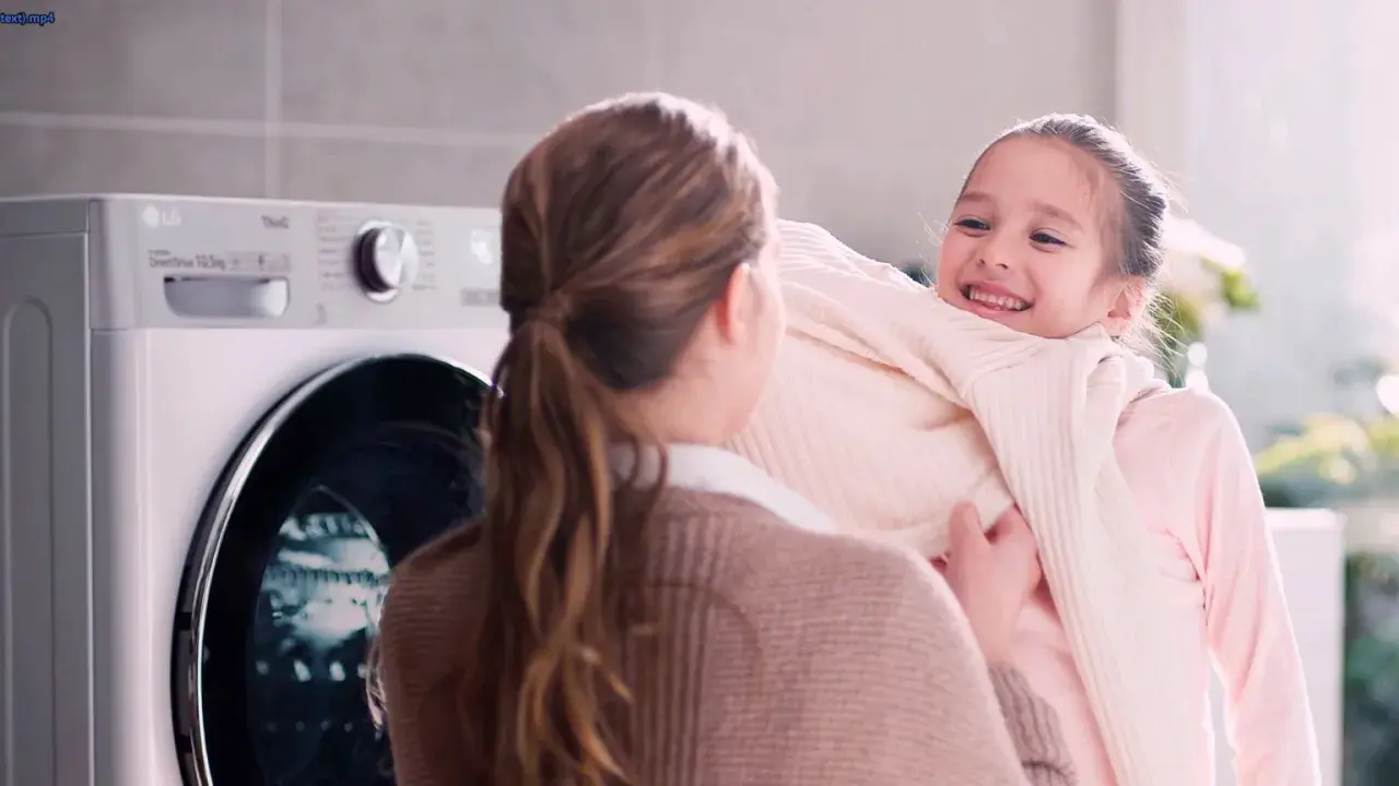 Bambina felice abbraccia maglione morbido, vicino a una lavatrice LG con funzione allergy care.