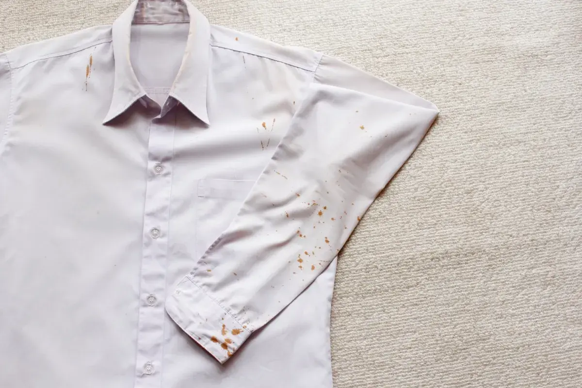 Camicia bianca con macchie di ruggine vecchie sui tessuti, soprattutto sulla manica e sul colletto.