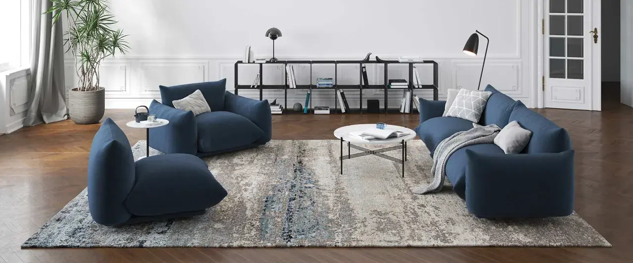 Un ampio tappeto 3 metri con motivi astratti grigi e blu, che completa un salotto moderno con divani blu e tavolino bianco.