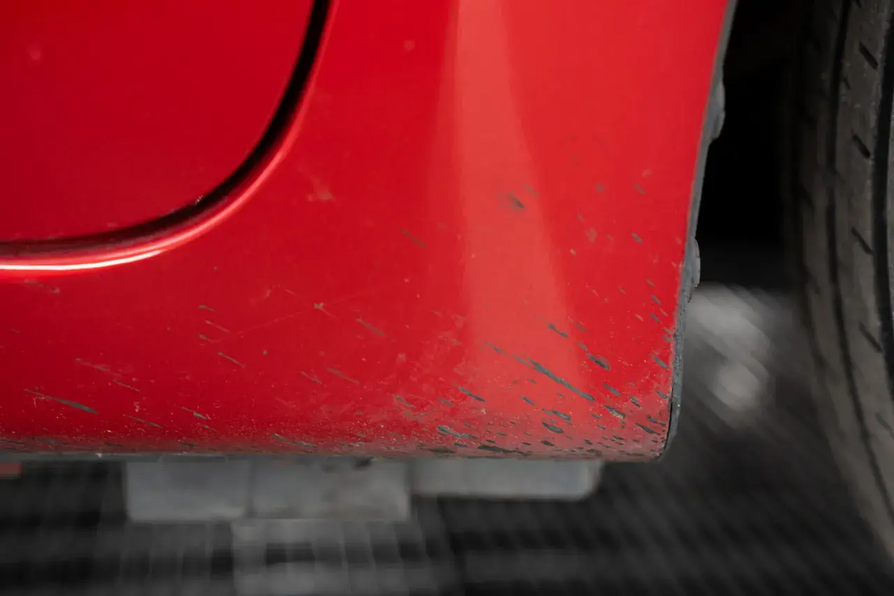 Macchie scure sulla carrozzeria rossa di un'auto, un problema comune per chi cerca come togliere le macchie di catrame.