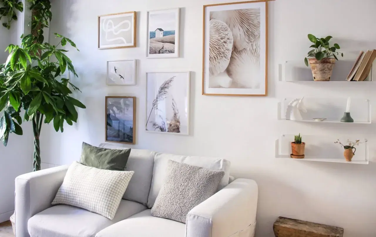 Galleria di quadri e mensole bianche sopra un divano bianco, con piante e oggetti decorativi. Idee mensole sopra divano per un tocco di stile.